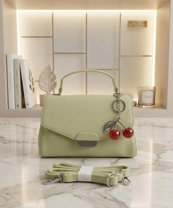 Light green handbag with cherry charm on a marble surface