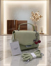 Light green handbag with cherry charm on a marble surface, accompanied by a strap and tag.