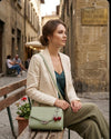 Woman sitting on a bench in an old street with a green handbag.