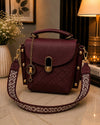 Maroon handbag with gold accents on a surface, with a decorative strap.