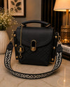 Black quilted handbag with gold accents on a marble surface, with a lamp and plant in the background.