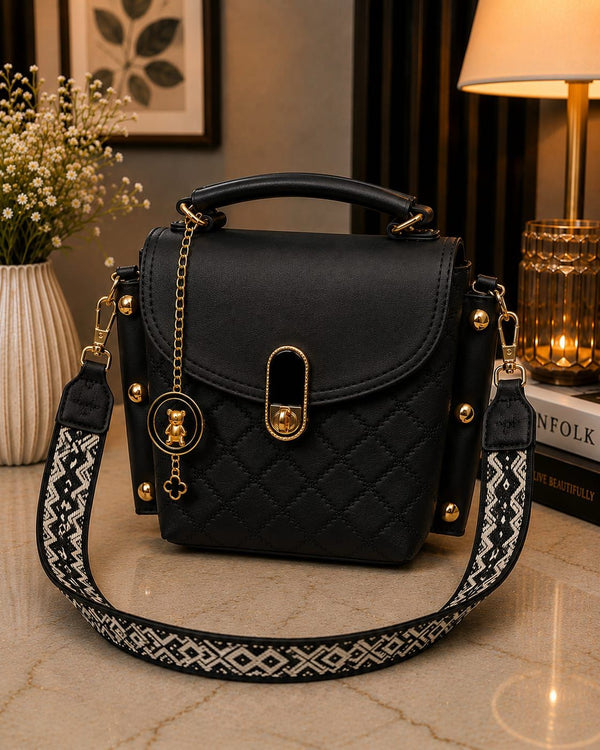 Black quilted handbag with gold accents on a marble surface, with a lamp and plant in the background.