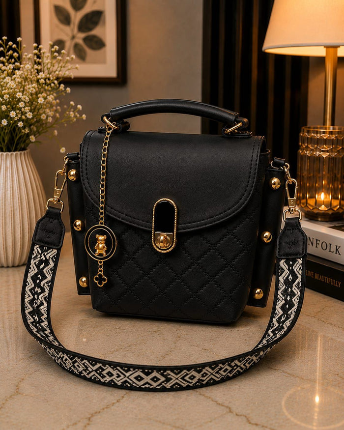 Black quilted handbag with gold accents on a marble surface, with a lamp and plant in the background.