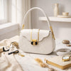 White handbag with gold accents on a marble surface with decorative items.